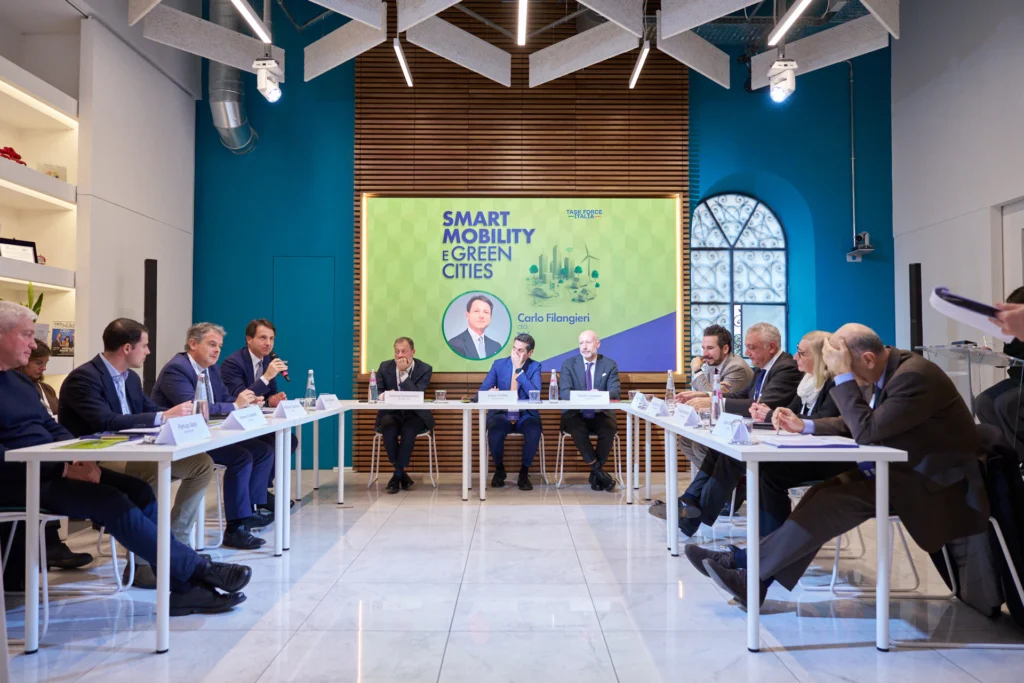 A group of people in a conference room sit around a U-shaped table, discussing "Smart Mobility & Green Cities." The tone is professional and collaborative.