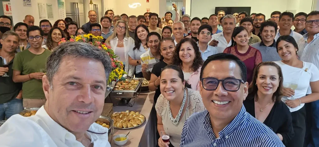 A group of smiling people at a social gathering pose for a selfie. A table with food and drinks is visible, creating a lively and joyful atmosphere.