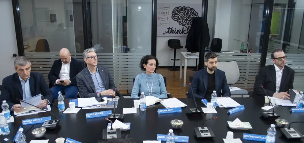 A group of six people sits at a conference table in a modern office. They appear engaged, with laptops and papers in front of them, conveying a focused and professional tone.