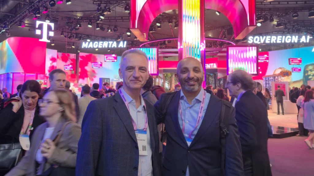 Two men smiling at a vibrant tech exhibit.. colorful neon lights, and a bustling crowd, conveying a lively and energetic atmosphere.