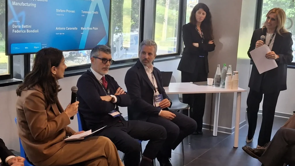 A panel discussion features five professionals seated and talking. One woman holds a microphone, engaging the audience. The atmosphere is focused and professional.