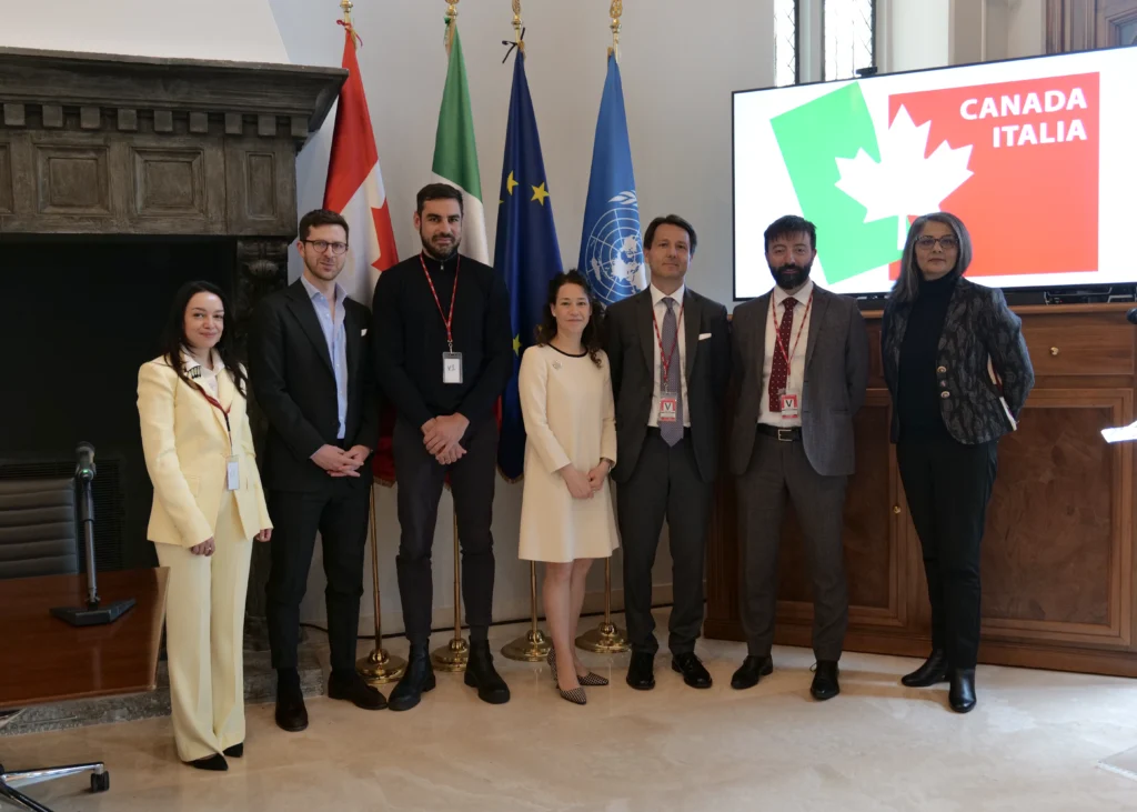 Seven people standing in the Canadian Embassy with flags behind them