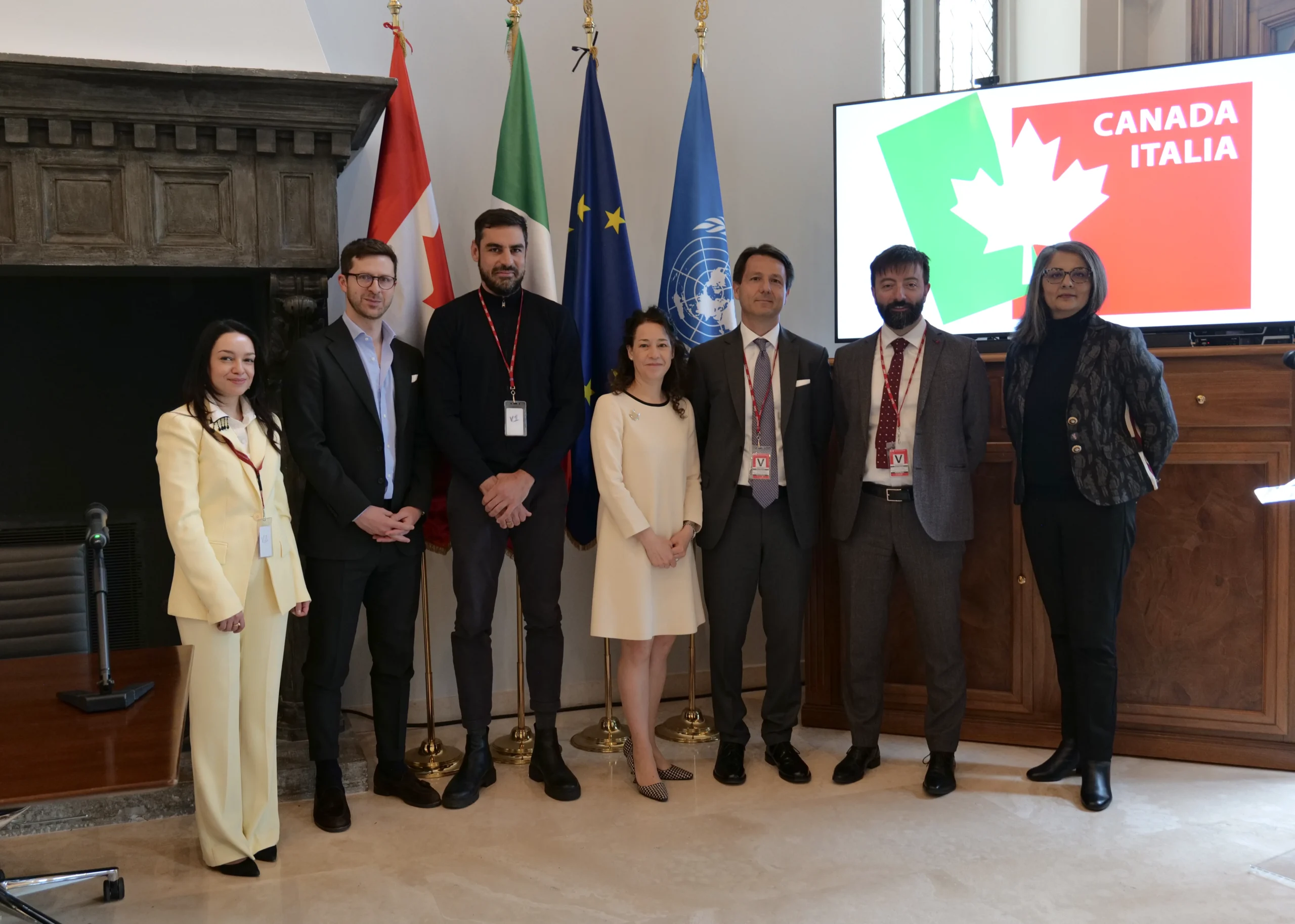 Seven people standing in the Canadian Embassy with flags behind them