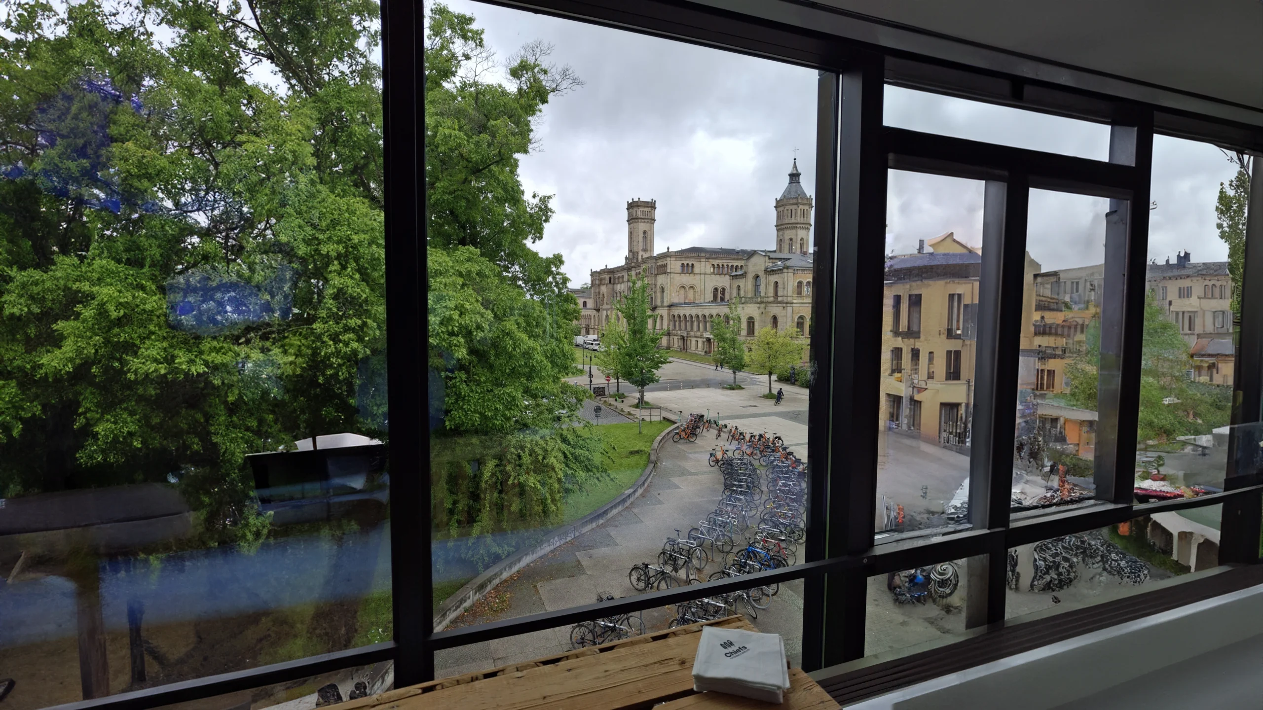 View from a modern building showcasing a city square with trees, historic architecture, and parked bicycles under a cloudy sky. It is Hanover University