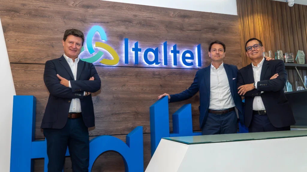 Three professionals posing confidently in front of the Italtel logo, showcasing a modern office environment and teamwork.