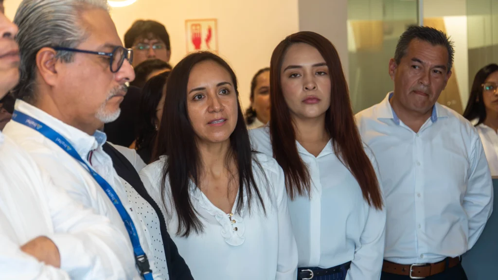 Close-up of a diverse group of business professionals listening attentively during a corporate meeting or workplace presentation. Office employees in white business attire standing together indoors, showing focused and serious expressions during a team discussion or company briefing. Professional workplace environment featuring men and women in a modern office setting, including an older man with glasses and lanyard, two women in white blouses, and male colleagues in the background. Corporate collaboration, employee engagement, leadership communication, and business team meeting concept.