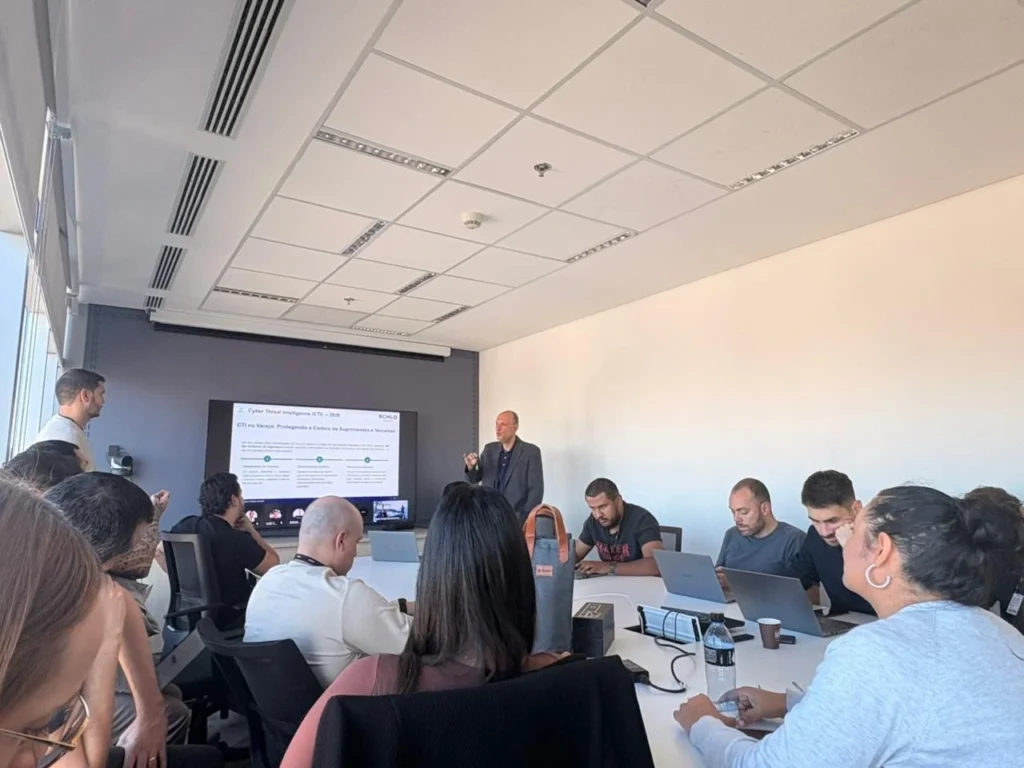 A business meeting with a speaker presenting on cyber threats, while attendees engage with laptops and notes in a modern conference room.