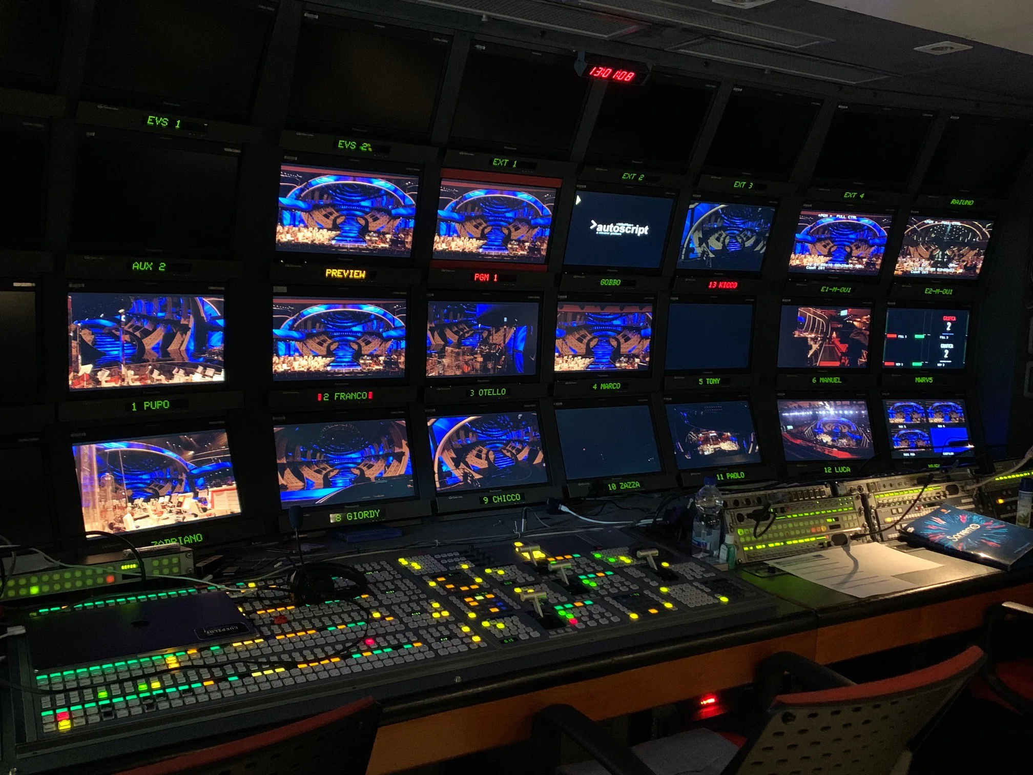 A television control room featuring multiple screens displaying a live event with colorful lighting and various control equipment.