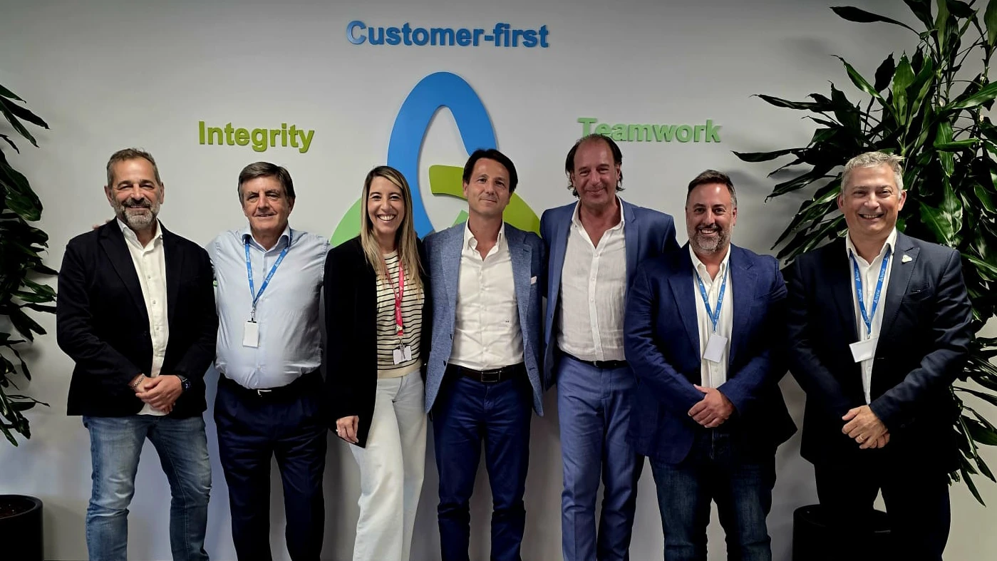 People of Italtel Spain with CEO  smiling in business attire, standing in front of a wall with words "Customer-first," "Integrity," and "Teamwork." The mood is positive and professional.
